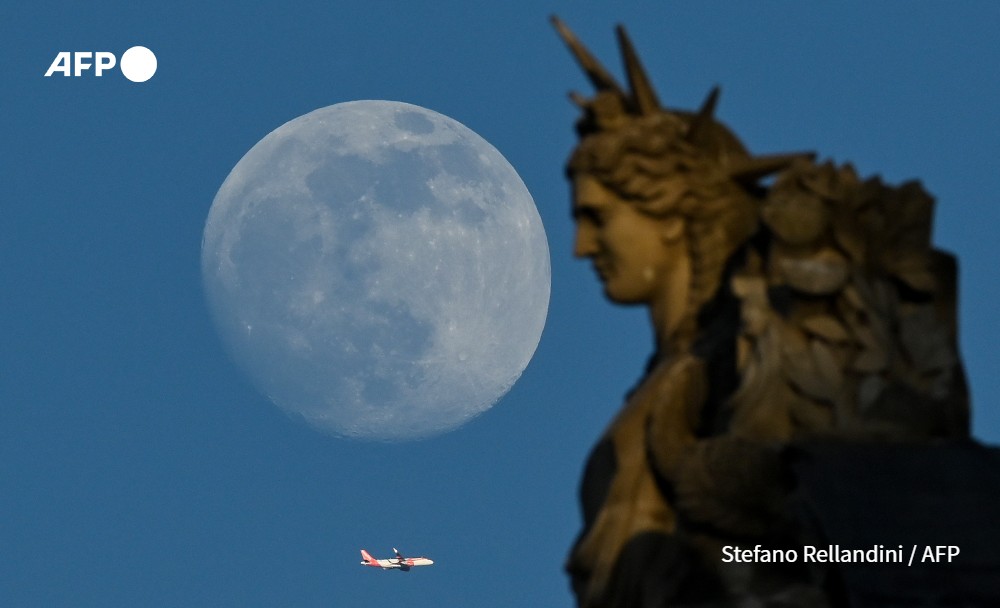 Plane flies by a statue of the Louvre, while the moon rises, Paris