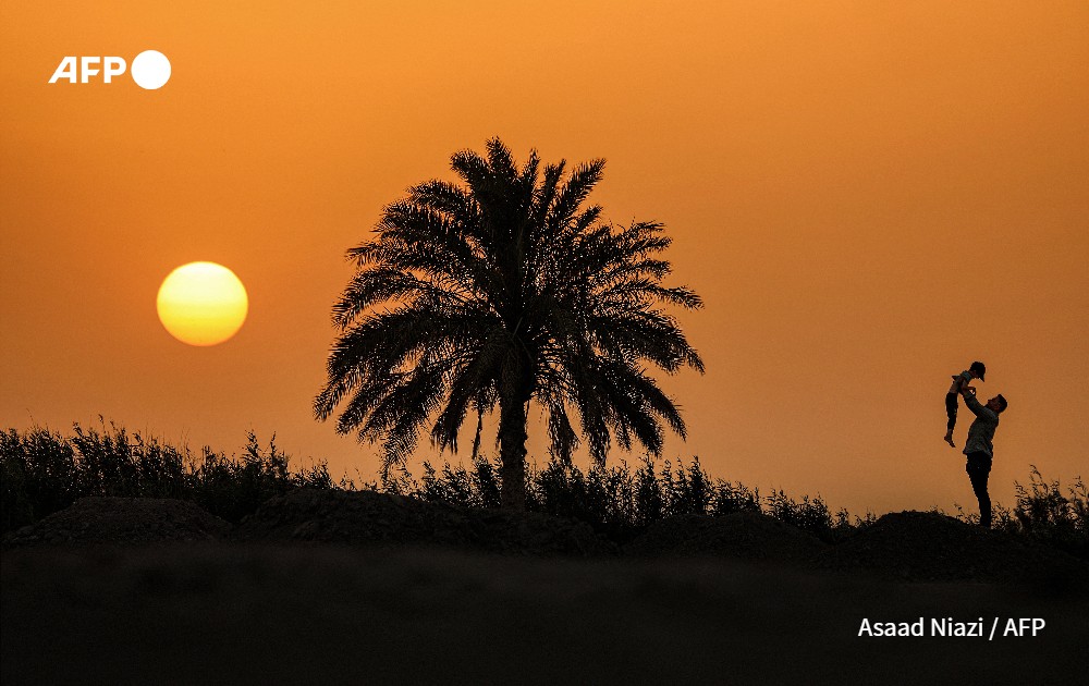 Man holds up a boy at sunset, Iraq