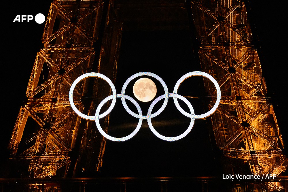 The moon rises behind the Olympic rings displayed on the Eiffel Tower in Paris