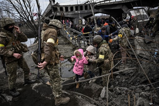 People cross a destroyed bridge as they evacuate the city of Irpin, northwest of Kyiv, during heavy shelling and bombing, 10 days after Russia launched a military invasion on Ukraine, on March 5, 2022