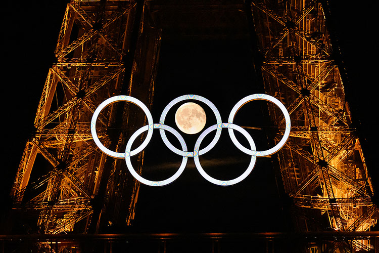 La lune se lève derrière les anneaux olympiques affichés sur la Tour Eiffel à Paris, le 22 juillet 2024, avant les Jeux Olympiques de Paris 2024. © Loic Venance / AFP