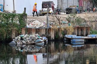 Cette photo montre un travailleur marchant à côté d'un tas de déchets plastiques sur une plateforme dans un canal à Phnom Penh. © Tang Chhin Sothy / AFP